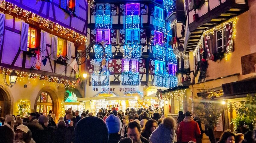 Half-timbered Alsatian building in Colmar illuminated at night during Christmas, adorned with festive decorations and lights.