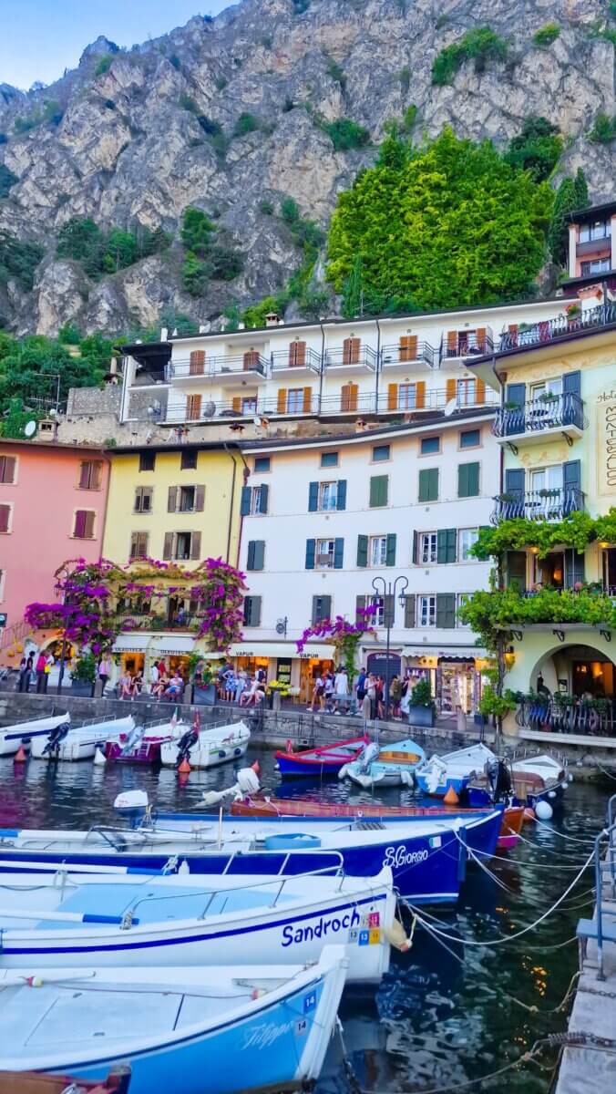 Discover the Most Beautiful Places Around Lake Garda Italy: Riva del Garda, Limone sul Garda, Malcesine and More Colorful waterfront buildings and small boats docked at the harbor in Limone sul Garda, Lake Garda, Italy.