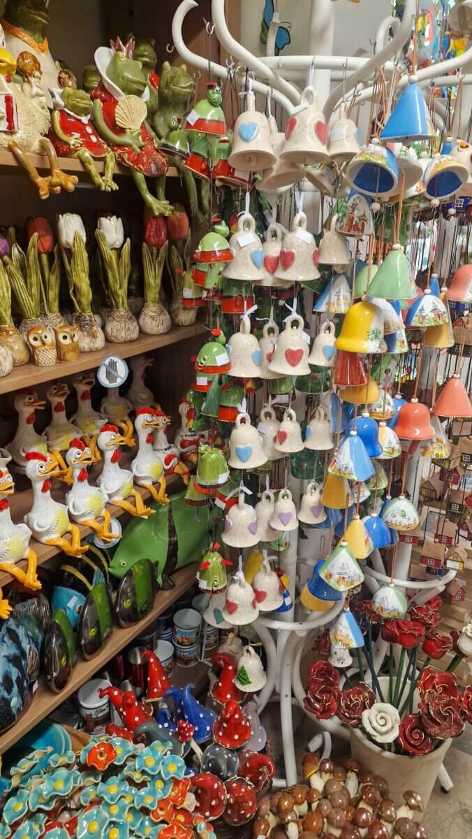 Display of colourful ceramic souvenirs in a shop, including bells, figurines of frogs and chickens, mushrooms, flowers, and other handmade decorations.