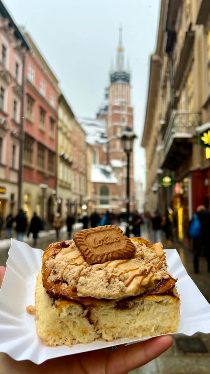 Lotus biscoff cinnamon roll on a street in Krakow city centre with St. Mary’s Basilica in the background