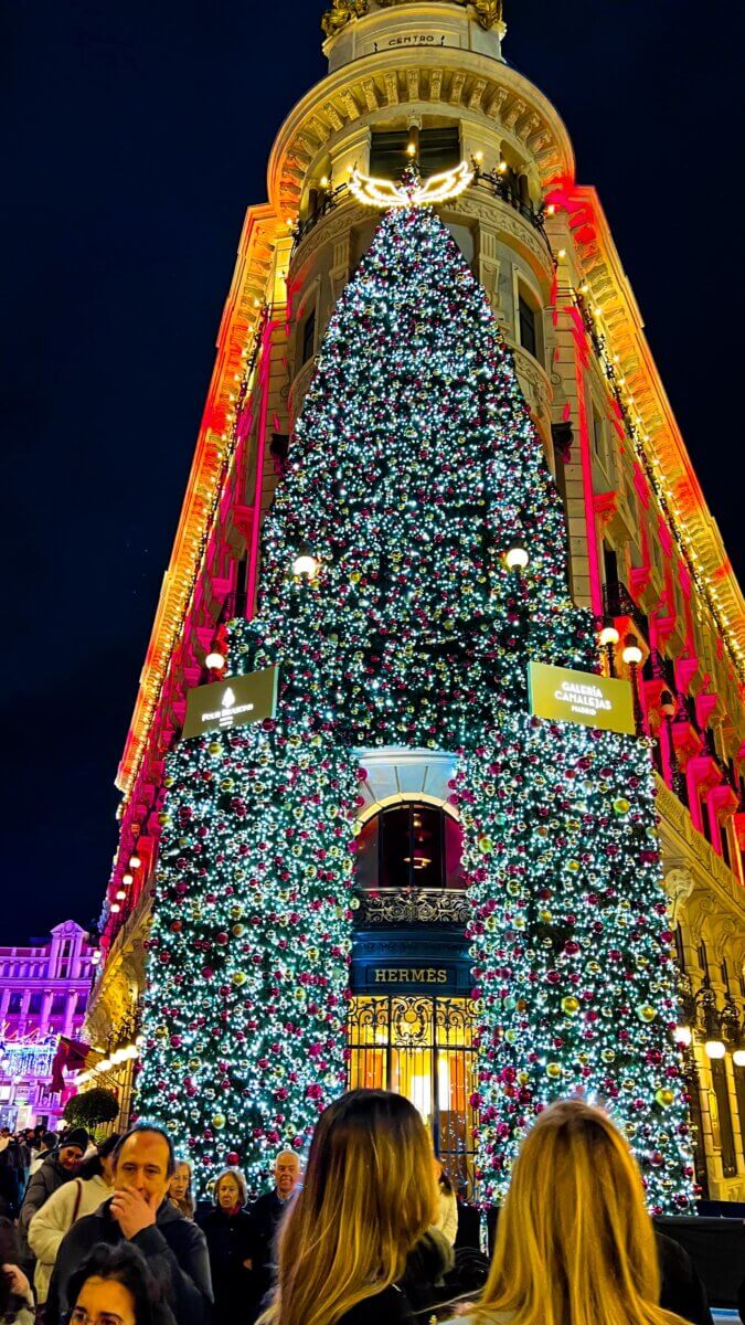 Hermès Christmas tree display at the Galería Canalejas in Madrid, Spain. The tree is located at the entrance of the luxury shopping center Galería Canalejas, which houses the Hermès store. This specific display is notable for its size and intricate lighting, featuring the Hermès brand name prominently above the entrance.