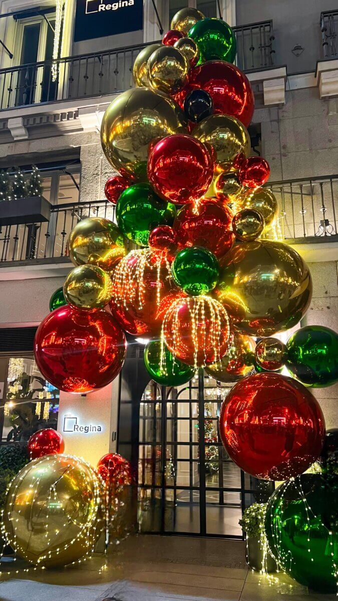 The image displays large, festive Christmas decorations outside the Hotel Regina in Madrid, Spain.