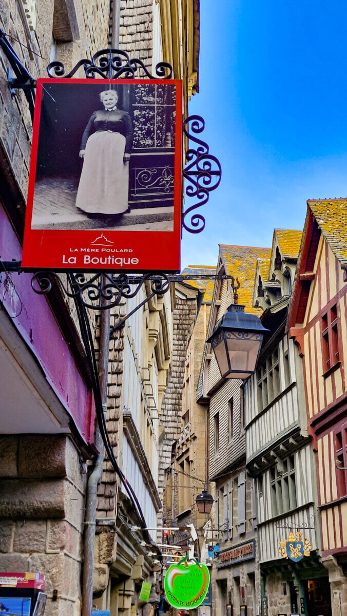 The scene shows a portion of the Grand Rue, the main steep, narrow cobblestone street lined with shops, cafes, and half-timbered houses