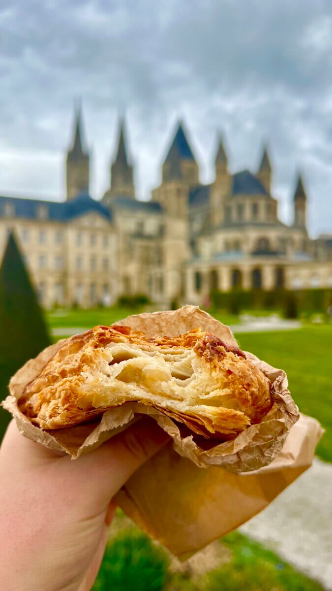 This moment captures an apple pastry, with the Abbaye-aux-Hommes (St. Étienne Abbey) in Caen, Normandy, France, blurred in the background