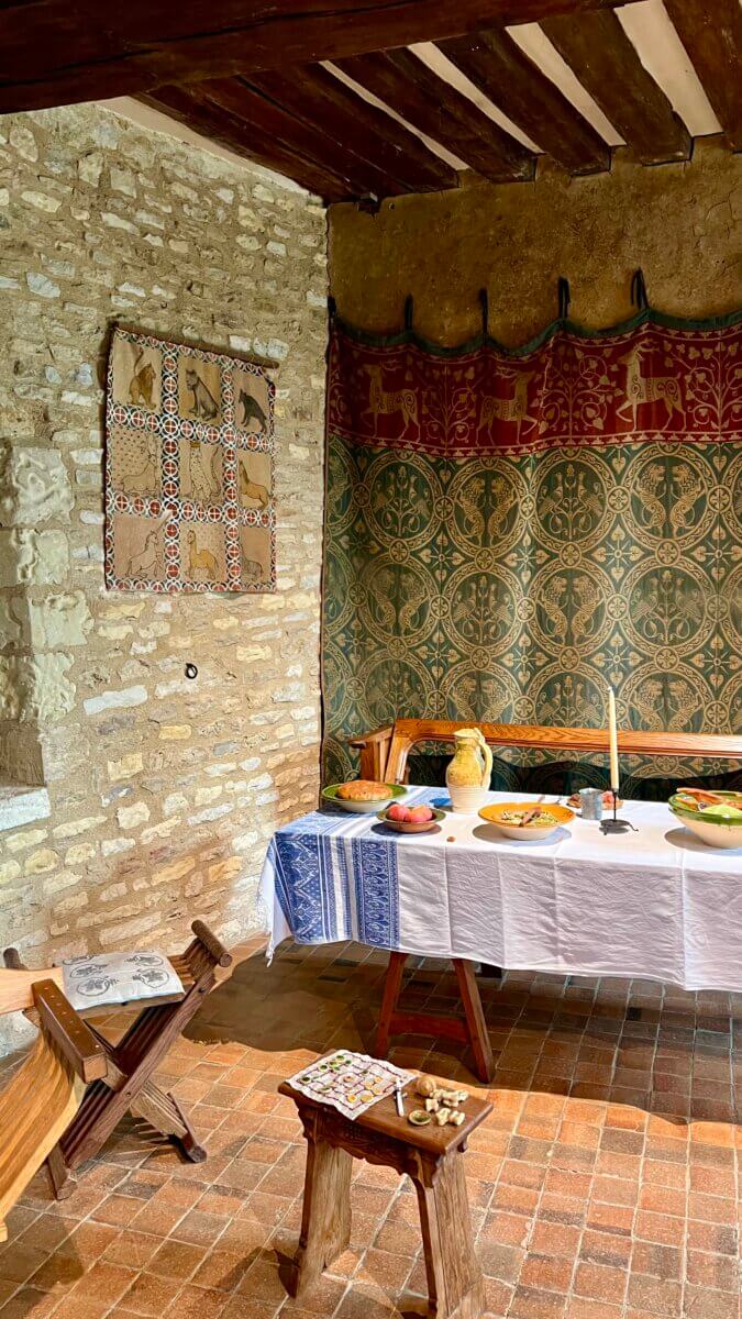 This scene depicts a historically styled interior at the Château de Crèvecœur in Normandy, France, showcasing a recreation of medieval life.