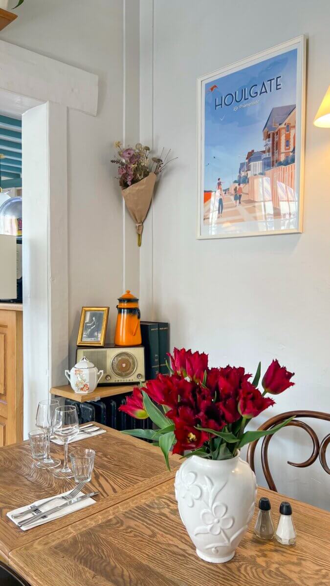 This is a charming dining scene featuring a vintage-style cafe interior with a "Houlgate" poster and a vase of red tulips on a wooden table