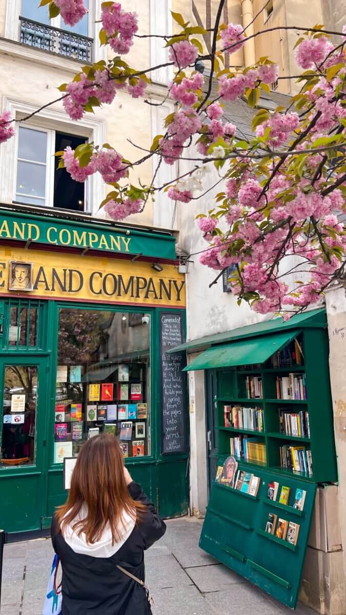 This image showcases the iconic Shakespeare and Company bookstore in Paris, decorated with vibrant pink cherry blossoms