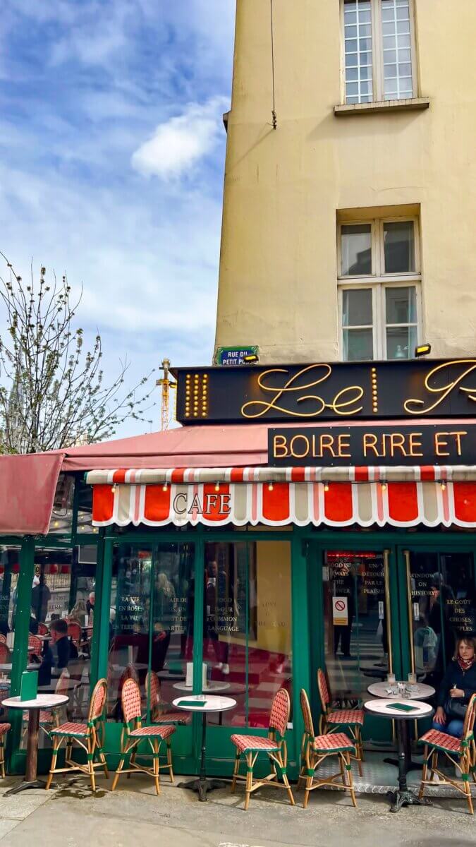 This is the terrace of the Le Petit Pont restaurant in Paris, featuring green chairs and red-and-white striped awnings