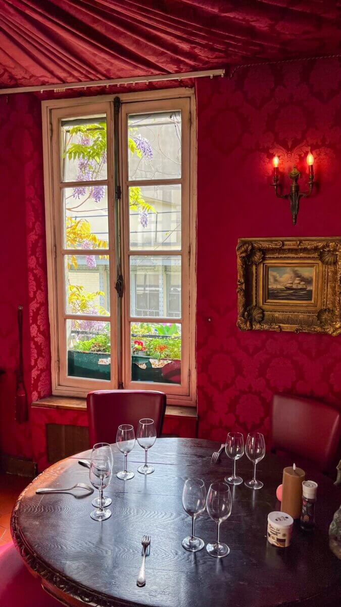 This vintage restaurant interior features crimson damask wallpaper and a dark wooden table setting