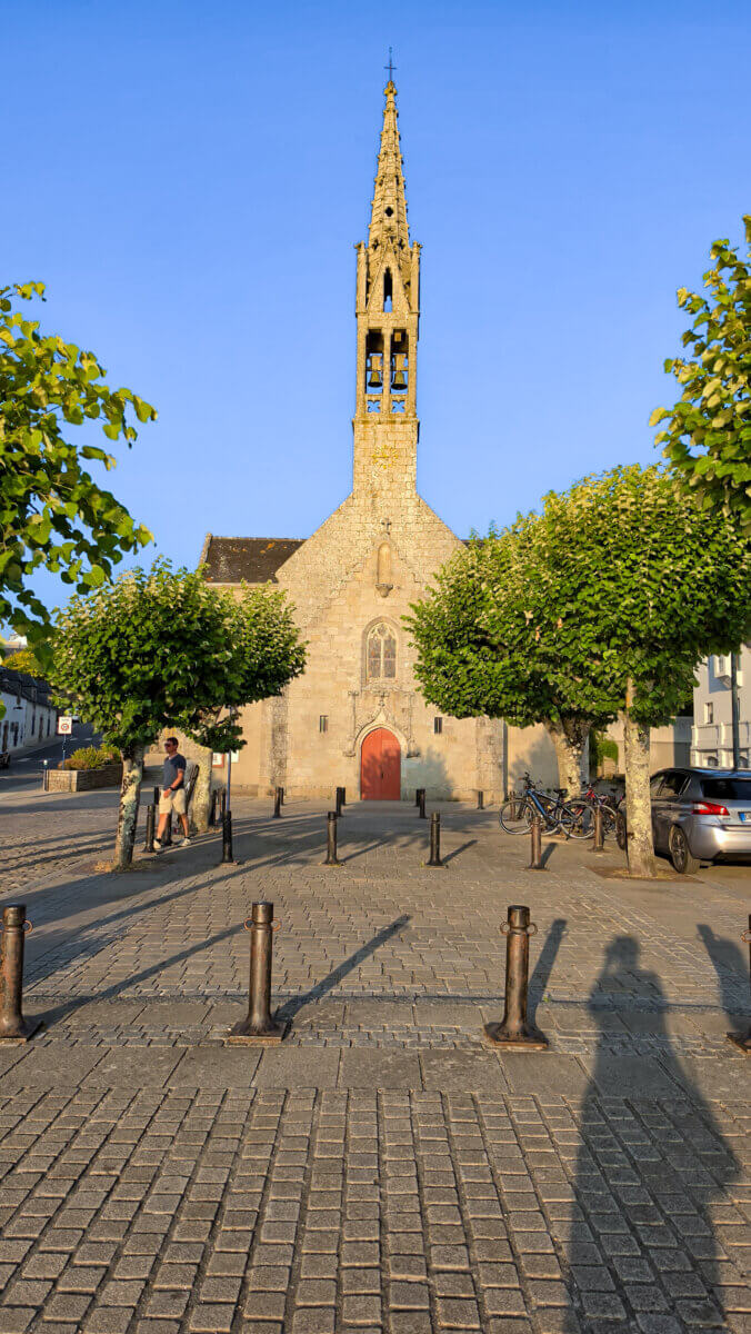The selected region displays the historic Église Saint-Thomas-Becket (also known as the Church of the Port) located in Bénodet, France. Its origins date back to a 13th-century chapel, featuring a distinctive stone bell tower and a prominent red-painted main entryway