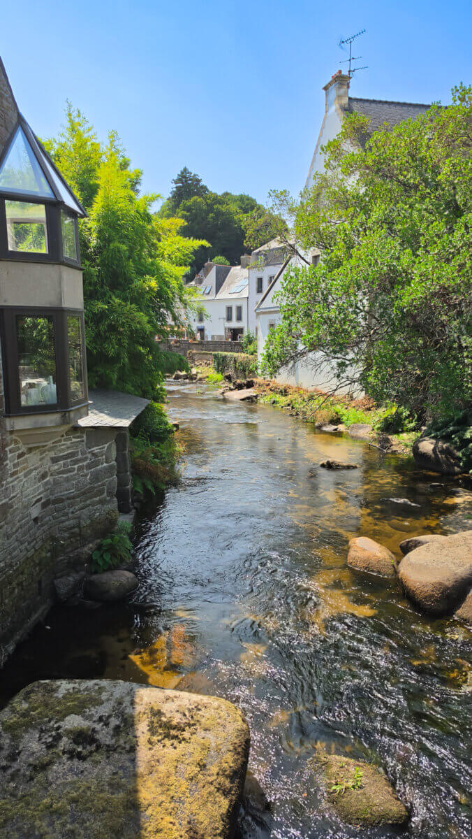 This scenic view shows the Aven River flowing through the historic village of Pont-Aven in the Finistère department of Brittany, France. Famous as an artists' colony where Paul Gauguin and other painters worked in the 19th century, the charming town is known for its stone buildings, lush greenery, and river walks