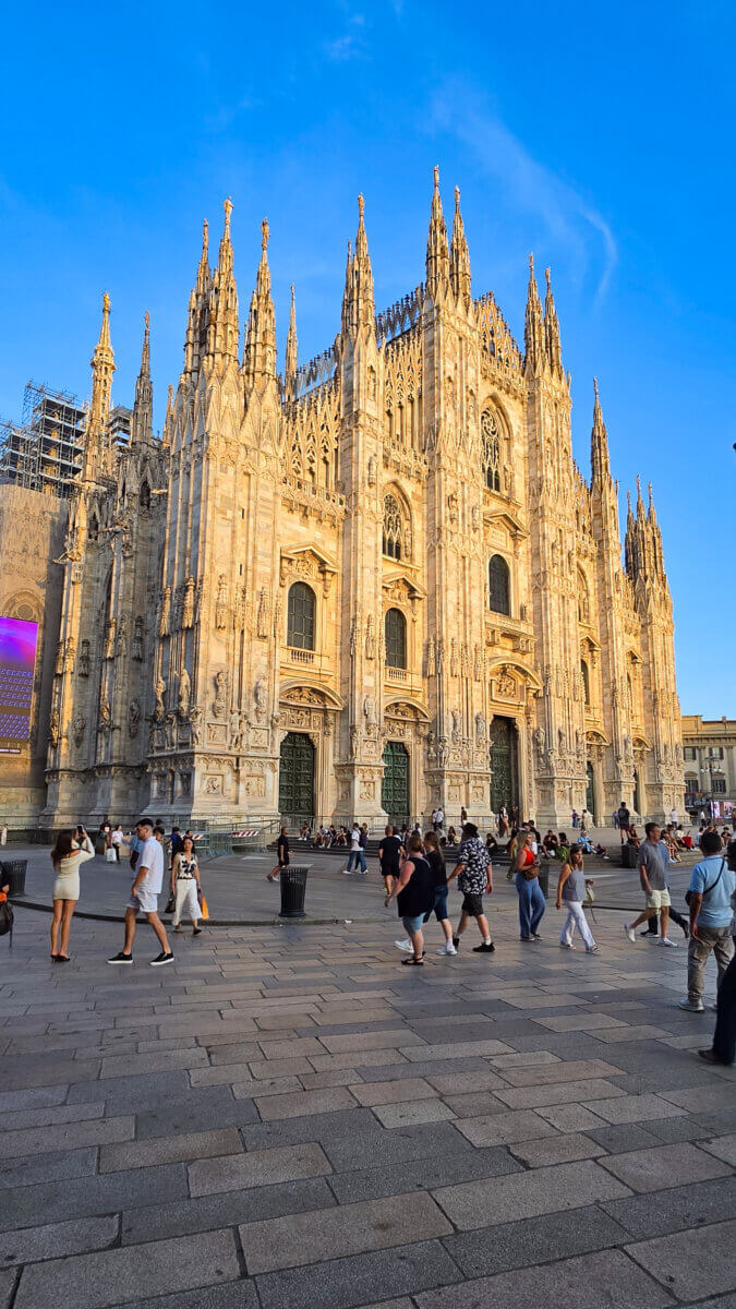 This image shows the magnificent Milan Cathedral, also known as the Duomo di Milano, standing in the busy Piazza del Duomo in Milan, Italy